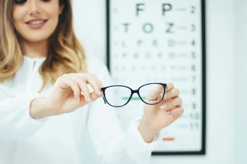 Optician holding up a pair of glasses in front of an eye chart